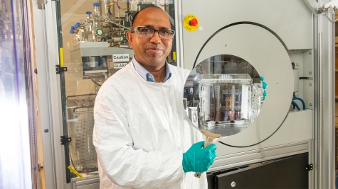 Argonne Senior Scientist Anil Mane holds a 300 mm silicon wafer coated by atomic layer deposition using the instrument in the background. (Image by Argonne National Laboratory.)